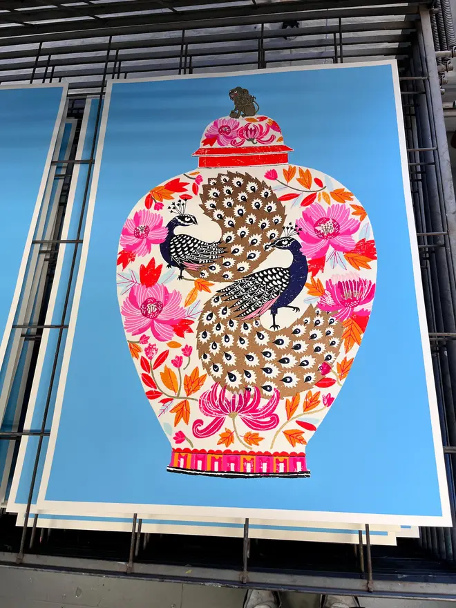 Peacock Vase Are You Looking At Me (You Probably Should), a colourful vase design on a blue screenprint, sitting against a studio rack. 