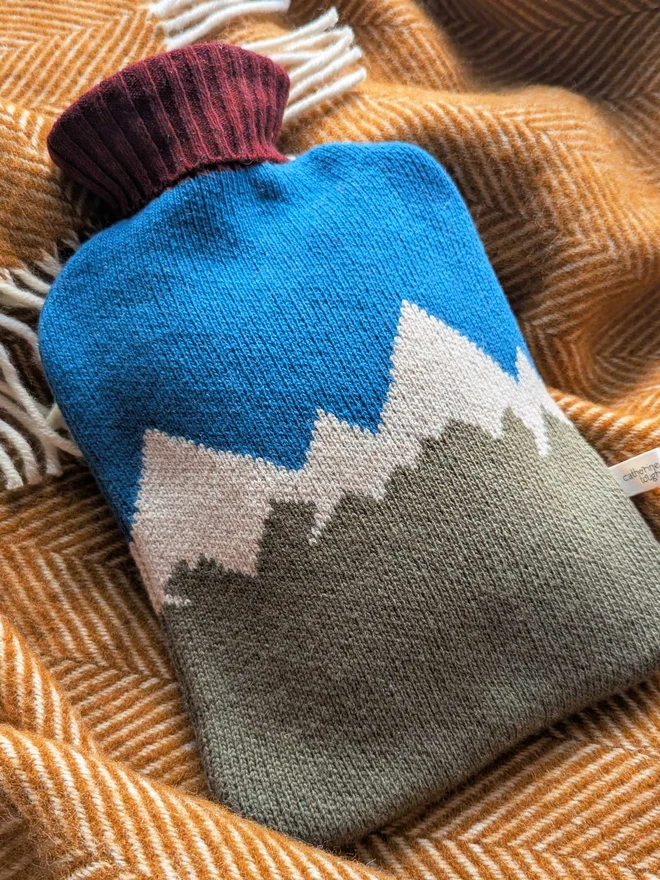 COLOURFUL HOT WATER BOTTLE COVER DISPLAYED ON A ON A BLANKET