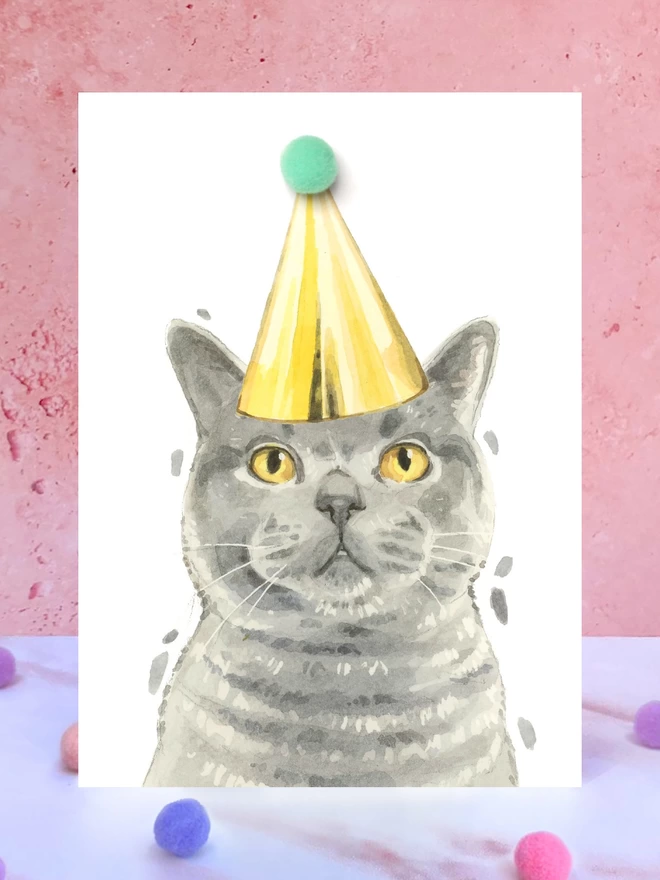 British Blue Shorthair Cat Pompom Birthday Celebration Collection Card in front of a pink background and surrounded by pompoms