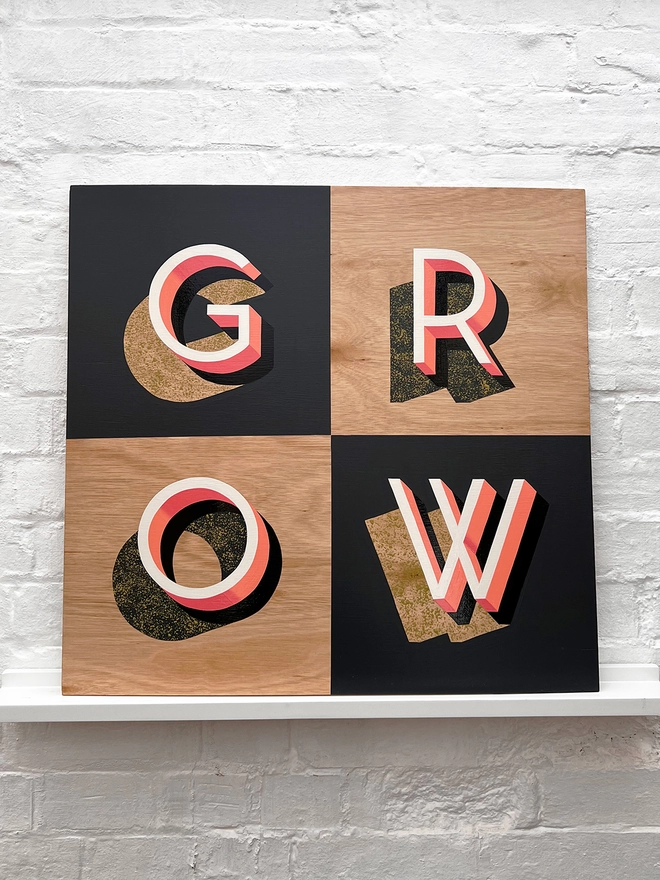 GROW hand painted sign in coral, dark grey and chartreuse, against a white brick wall, straight on.