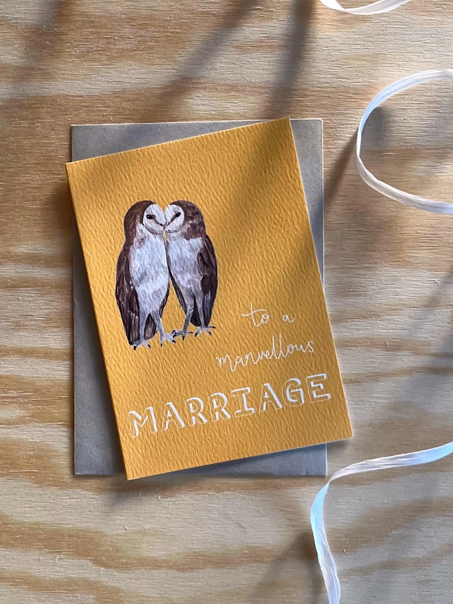 a greetings card with a bright yellow background featuring two kissing barn owls and the phrase ‘to a marvellous MARRIAGE”