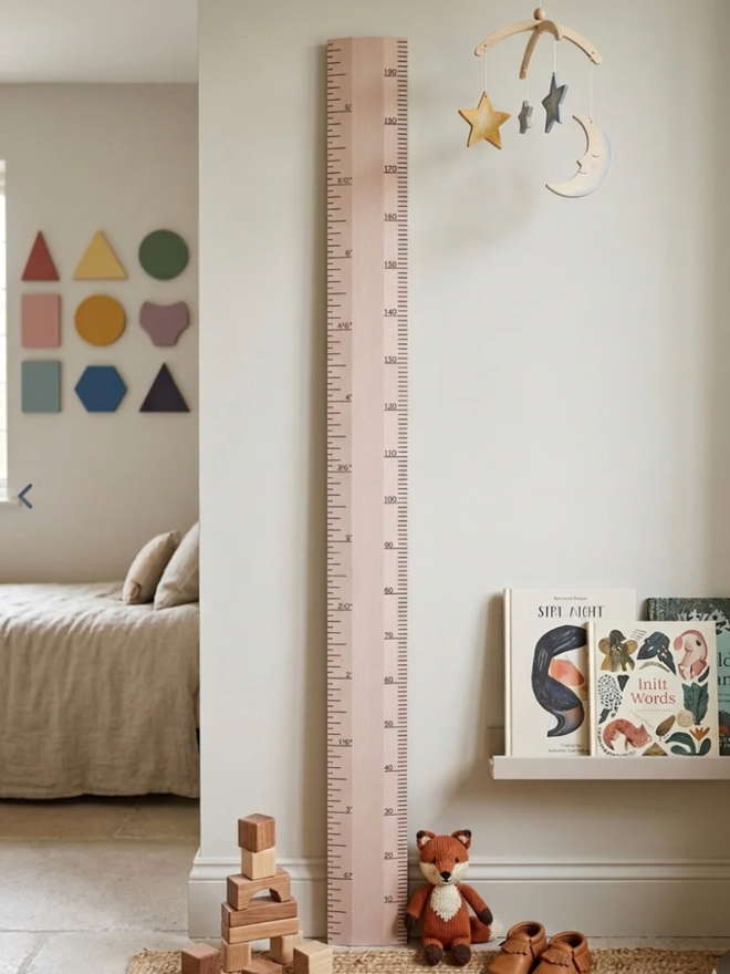 Wooden Height Chart. A large ruler height chart in Calamine Pink leaning against a child’s wall.