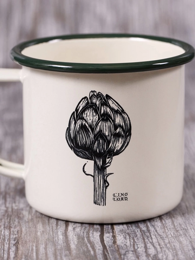 Picture of a Cream Enamel Mug with a Green Rim with an artichoke design etched onto it, taken from an original Lino Print