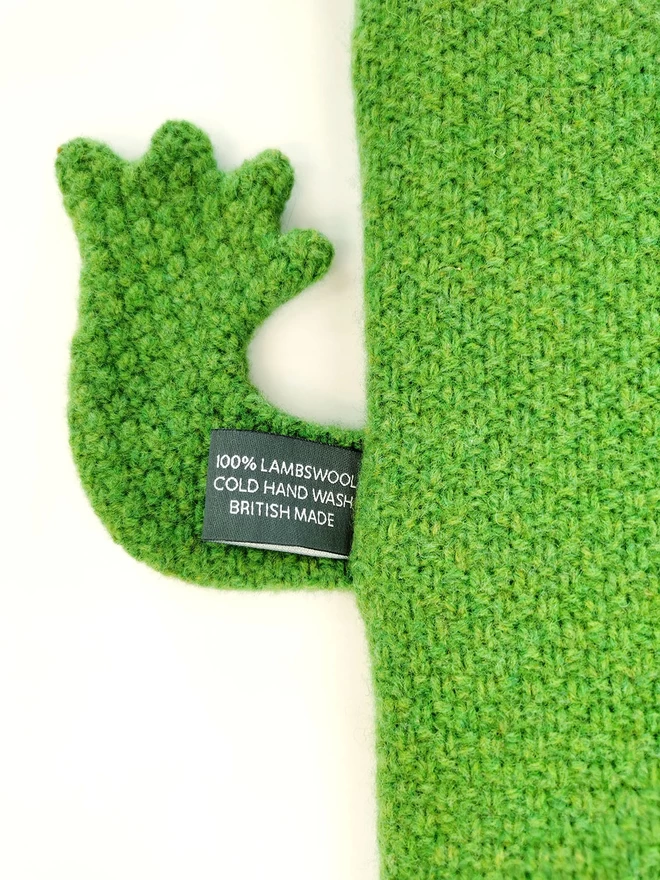 A close up of the underside of Claude the crocodile hot water bottle showing the textured lambswool knitted moss stitch fabric and care label.