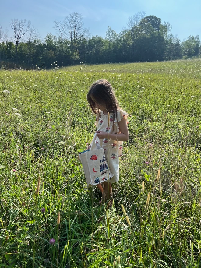 Girl in field in sunlight with small children's canvas bag