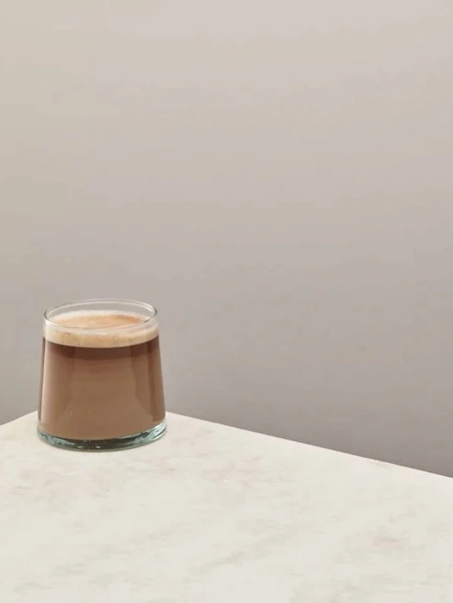 Low Glasses (Set Of 1 Or 4), a low glass sitting on a white counter top against a plain backdrop. It is filled by a soft drink. 