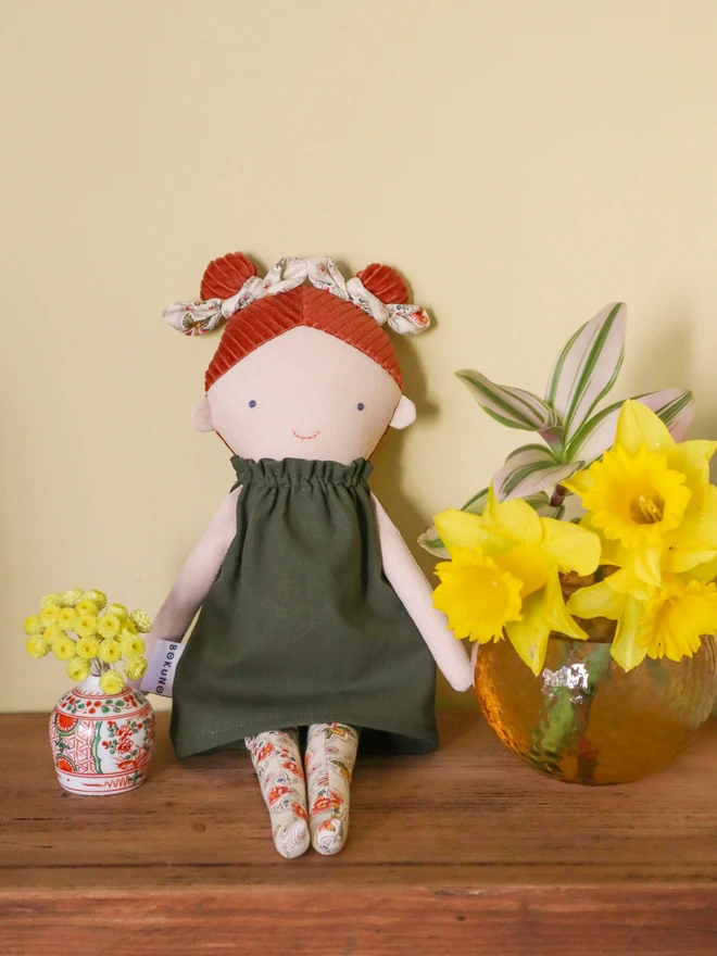 Handmade linen doll with light skin wearing dark green cotton dress and cream floral bows and tights. It has braided red hair made with corduroy.