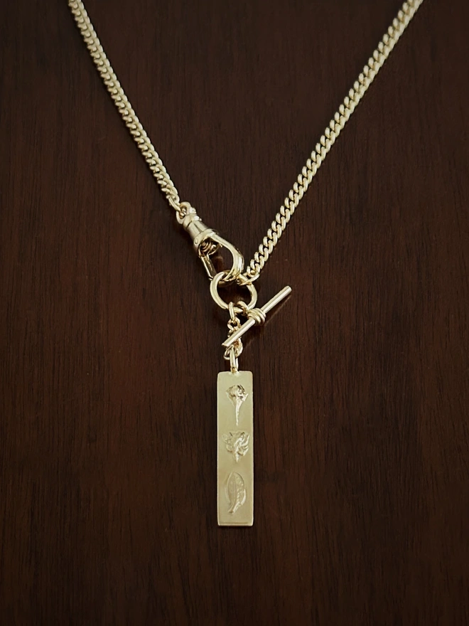 Gold plated sterling silver watch chain with a bar pendant to represent daughterhood on a dark background