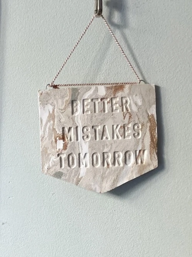 'Better Mistakes Tomorrow' Banner, a clay banner hanging against a plain backdrop.