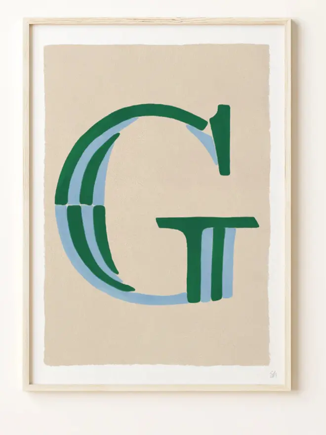 Framed wall art print featuring a large decorative letter “G” in humbug stripes
centered on a white background. 