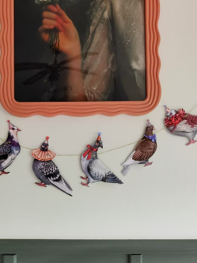 party pigeons circus garland. a string of paper pigeons in party and circus hats hung up on a wall.