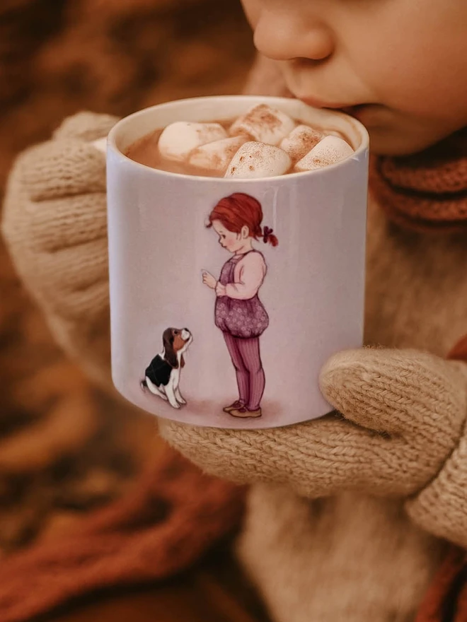 a child sipping hot chocolate from a small ceramic childs mug illustrated with a sweet red haired girl and a puppy Beagle illustrated in a vintage childrens book style lilac in colour