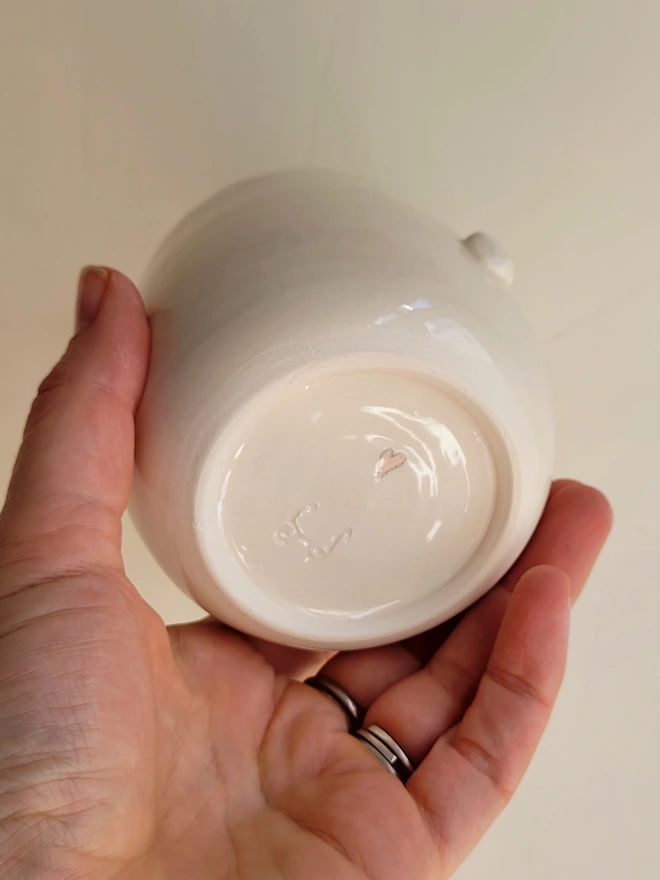 the base of a white ceramic cup with a pink heart underneath being held in a hand