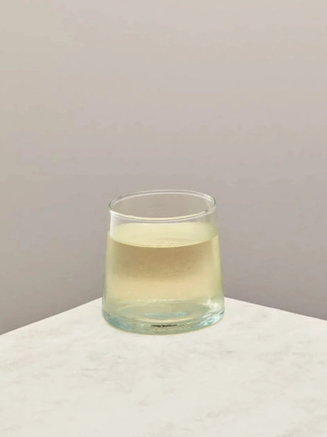 Low Glasses (Set Of 1 Or 4), a low glass sitting on a white counter top against a plain backdrop. It is filled by a soft drink. 
