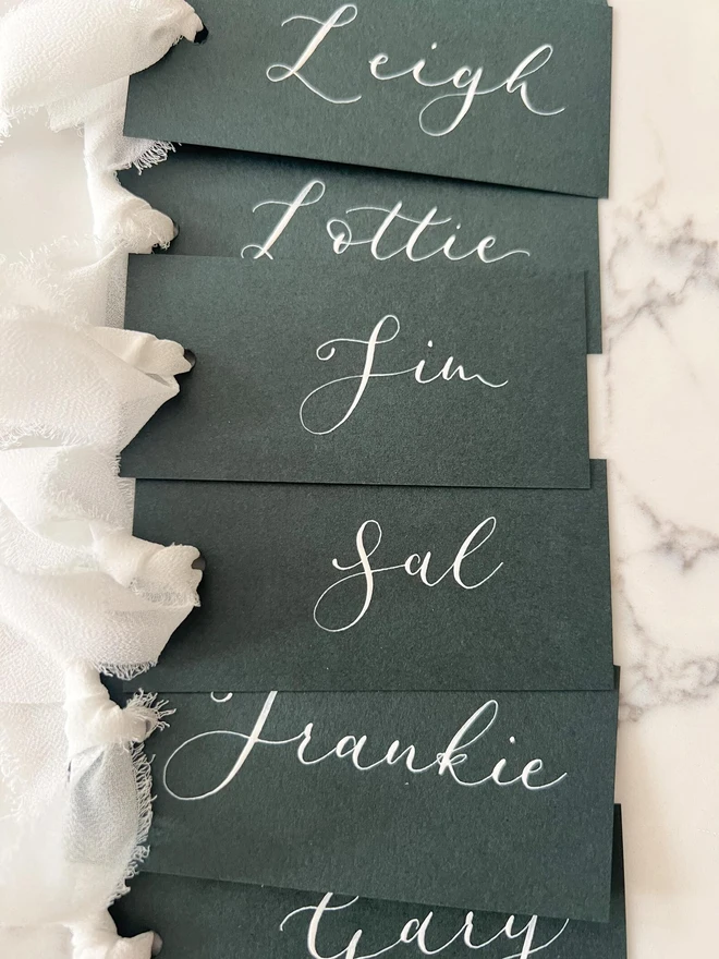 Personalised Calligraphy Wedding Forest Green Place Cards, grouped together with white ribbon. 