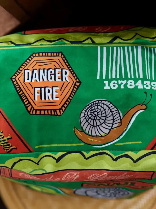 Snail Matchbox Cushion, a green decorated cushion sitting on a decorated surface. 