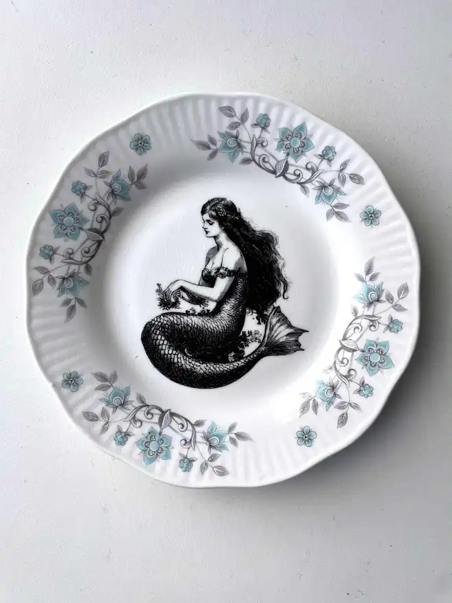 vintage plate with an ornate border, with a printed vintage illustration of mermaid in the middle 