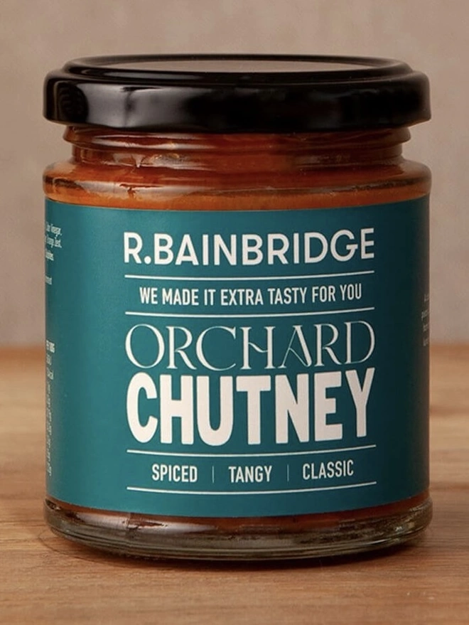 Orchard Chutney (Set Of 1, 2 Or 3), a jar of chutney sitting on a wooden surface against a plain backdrop. 
