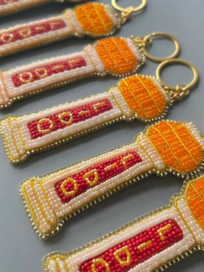 Multiple beaded lido key rings with orange, red, and beige beads line up in a row, against a plain background. 