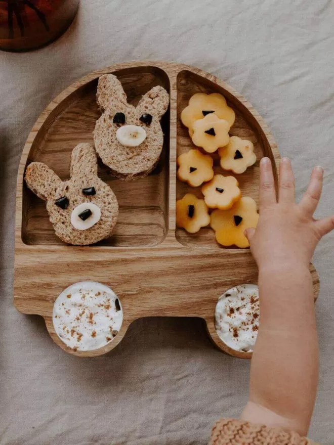 Eco wooden car plate filled with sandwiches and fruit in shapes of bunnies and flowers with dip filled in the two wheel holes birdseye view