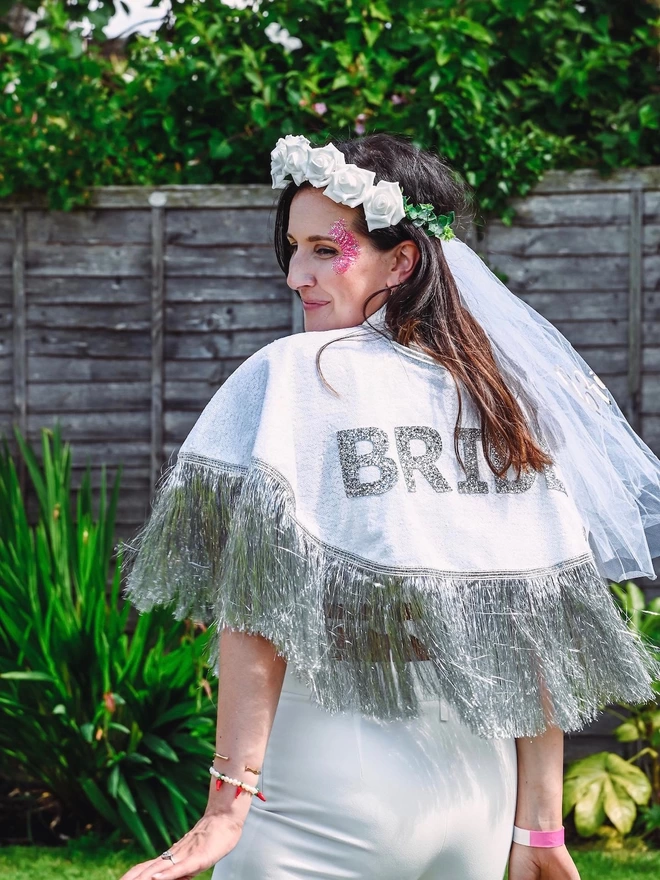 Another angle of a woman wearing the gretna bride cape. She is wearing a veil and pink face glitter.
