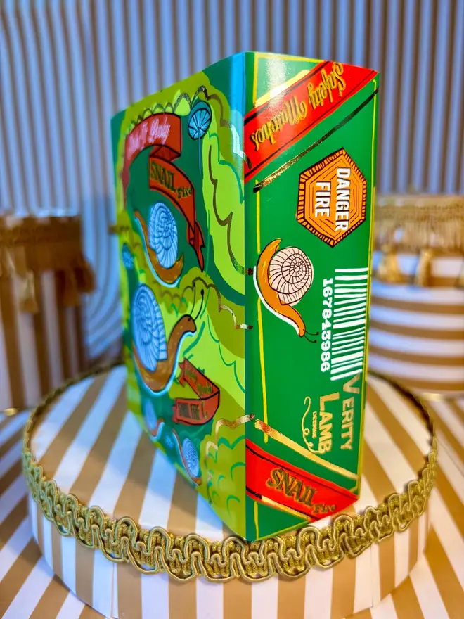 Snail Matchbox, a snail matchbox with a green design sitting on a decorated surface accompanied by other accessories.