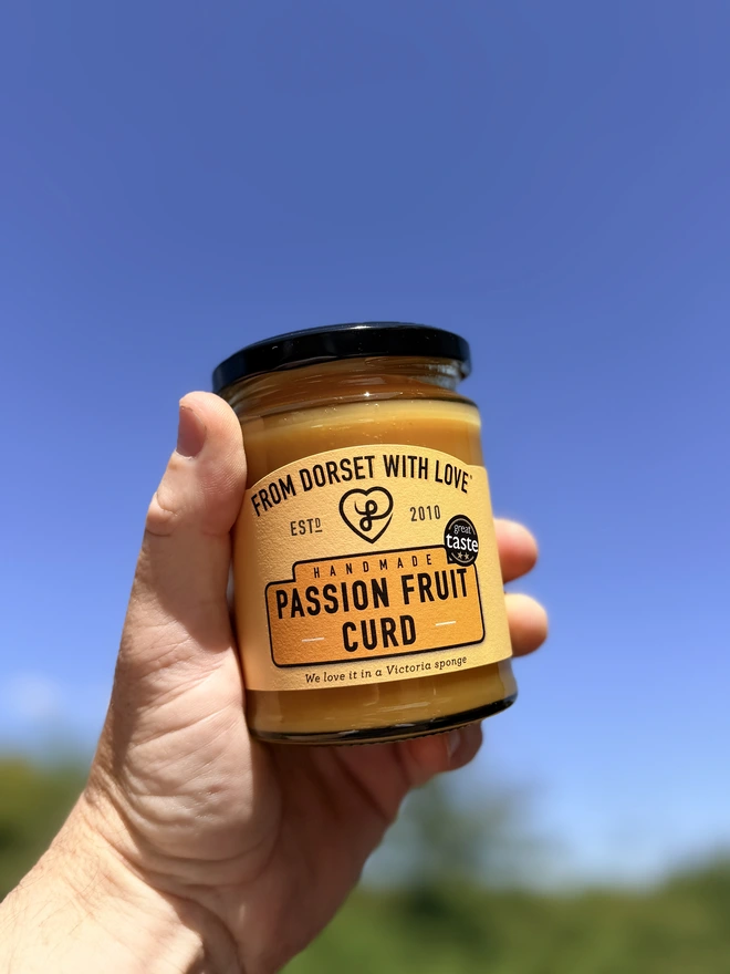 a hand holding a jar of passion fruit curd against a clear blue Dorset sky