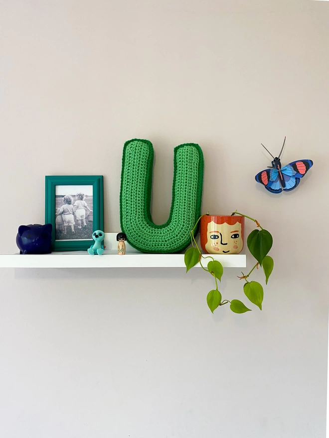 Crocheted U Cushion in Sage Green and Grass Green, on child's shelf