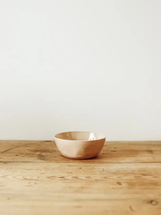 'sunrise' handcrafted stoneware bowls. a small pink bowl on a wooden bench.