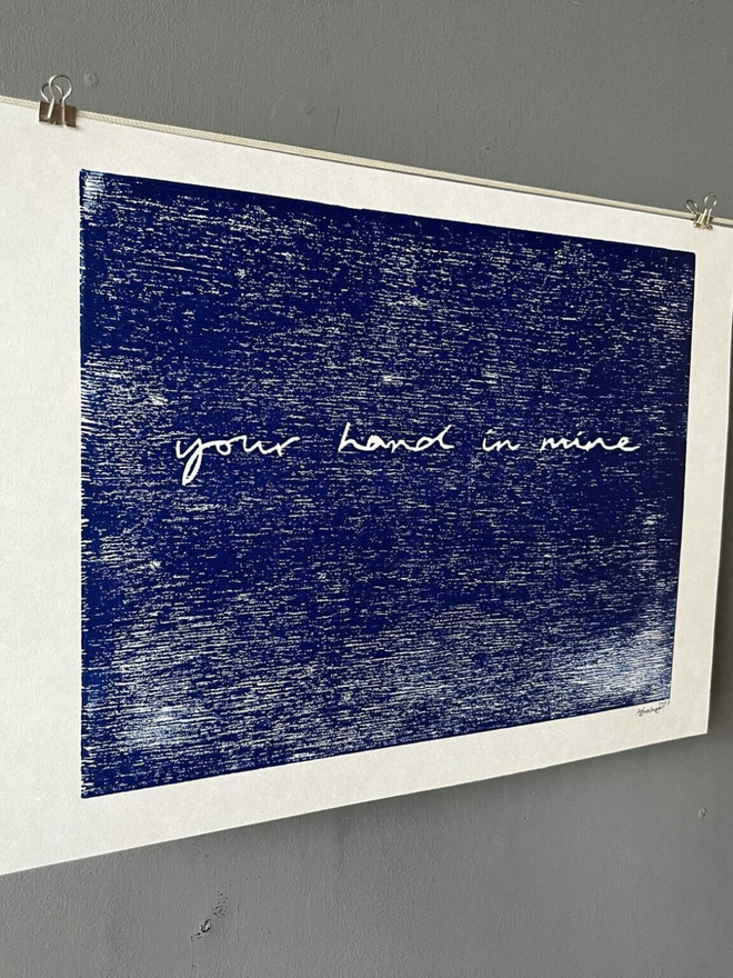'Your Hand In Mine' Letterpress Print hanging on a string against a grey wall