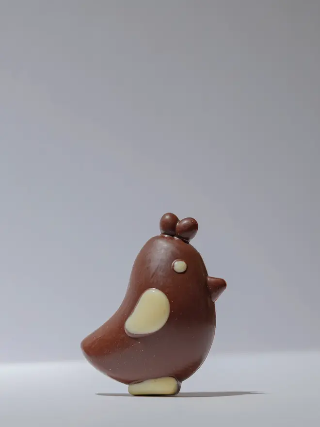 Solid milk chocolate chick with white chocolate wing and base detail, standing upright on a plain white background.