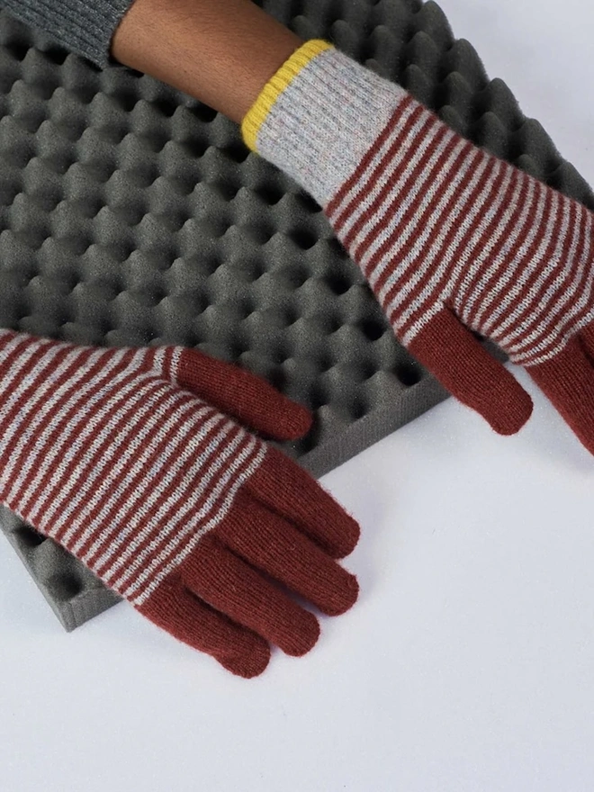 Block Lambswool Gloves, a person wearing a pair of colourful striped gloves above a table surface. 