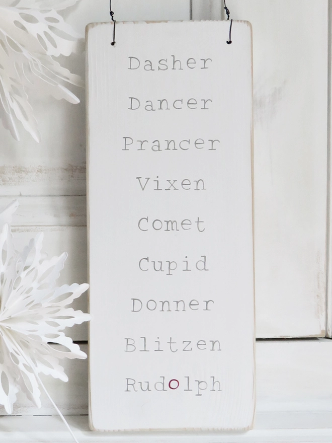 white painted wooden sign with reindeer names strung with wire and decorated with ribbon