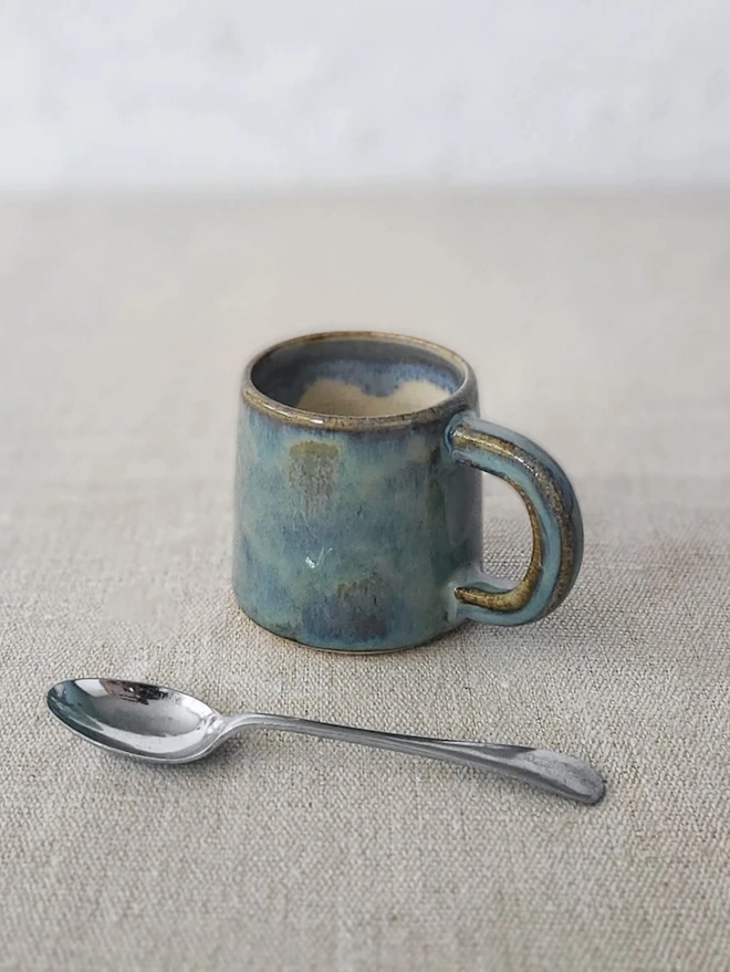 Classic Ceramic Espresso Mug, a colourful ceramic espresso mug sitting on a plain surface against a white backdrop. It is accompanied by a spoon. 