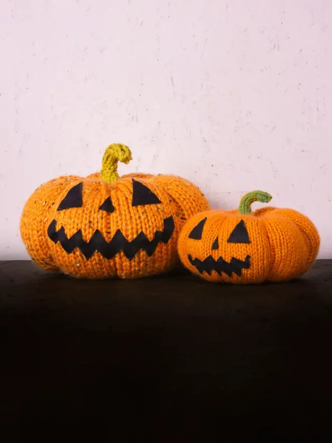 two knitted pumpkins, both with jack o lantern faces on table with black table cloth
