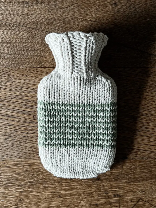 Mini Hot Water Bottle with green striped knitted string cover on an oak table