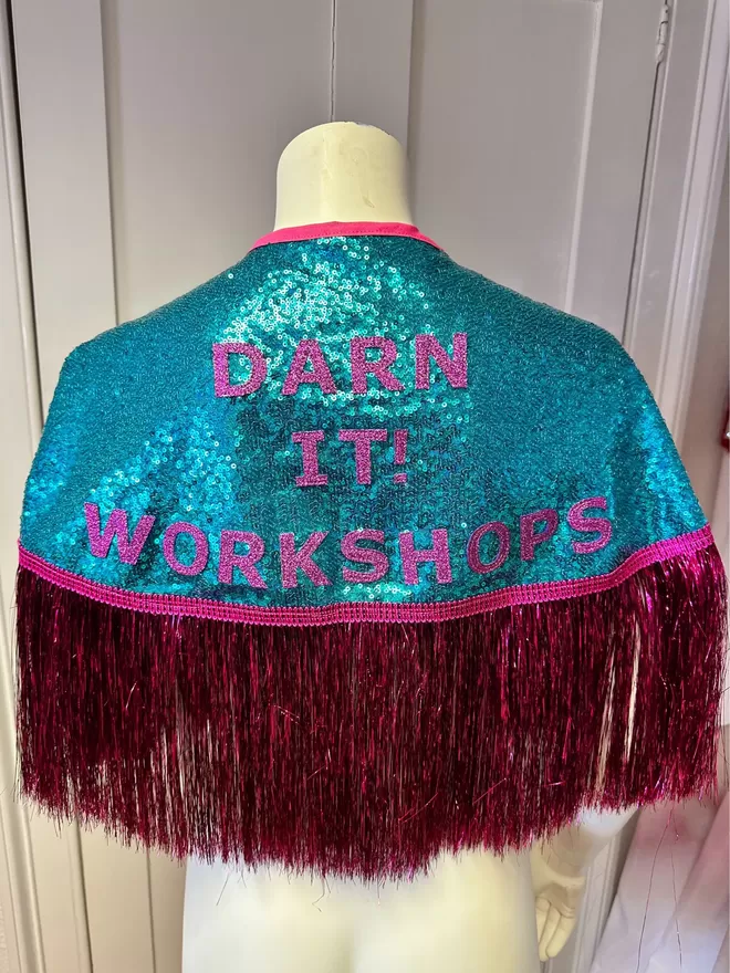 a midi cape with turquoise sequins, magenta text reading 'DARN IT! WORKSHOPS' and hot pink tinsel
