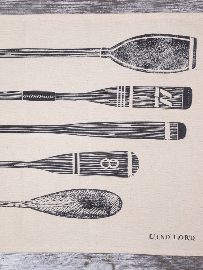 Picture of a tea towel with an image of oars and paddles, taken from an original lino print