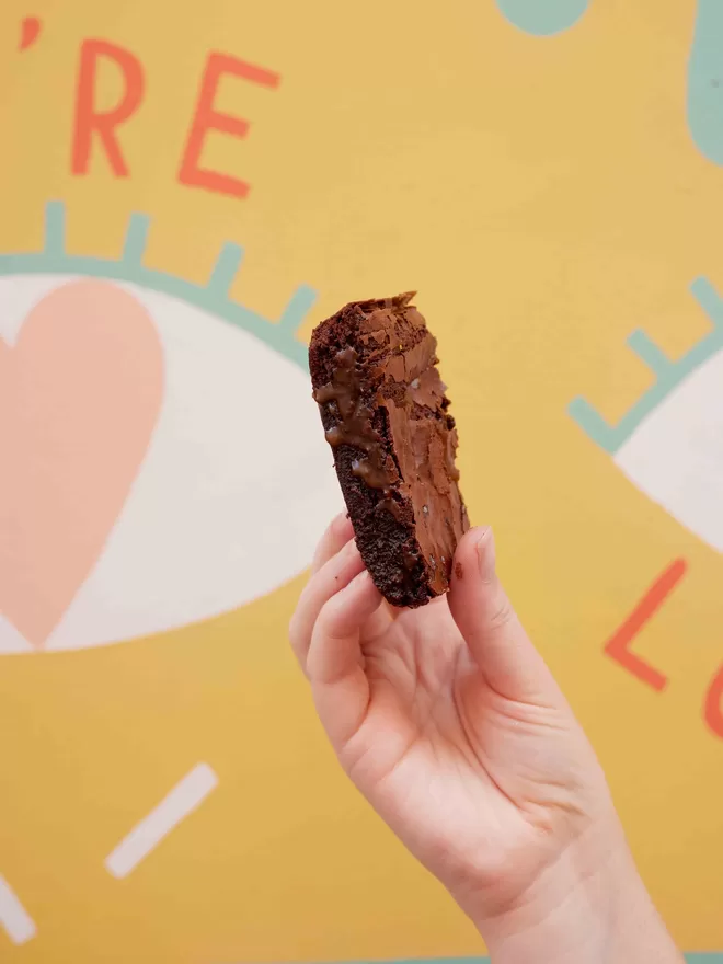 Single slice of sea salted caramel brownie being held in front of a colourful background