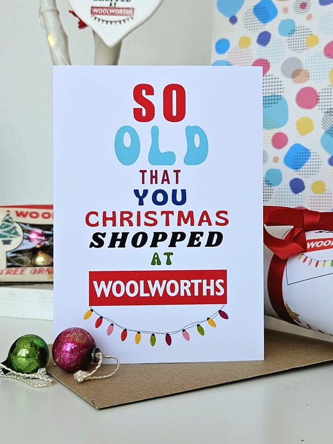 A photograph of the front of a humorous A6 greeting card illustrated using brightly coloured text and the retro shop logo. The text says so old you Christmas shopped at Woolworths with string lights