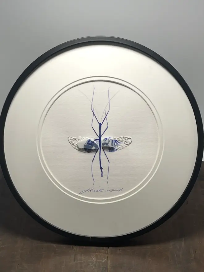 Hand-drawn, painted, mosaic clay, vintage blue Willow Tree pottery insect on white double mounted card, in a black circular frame.
