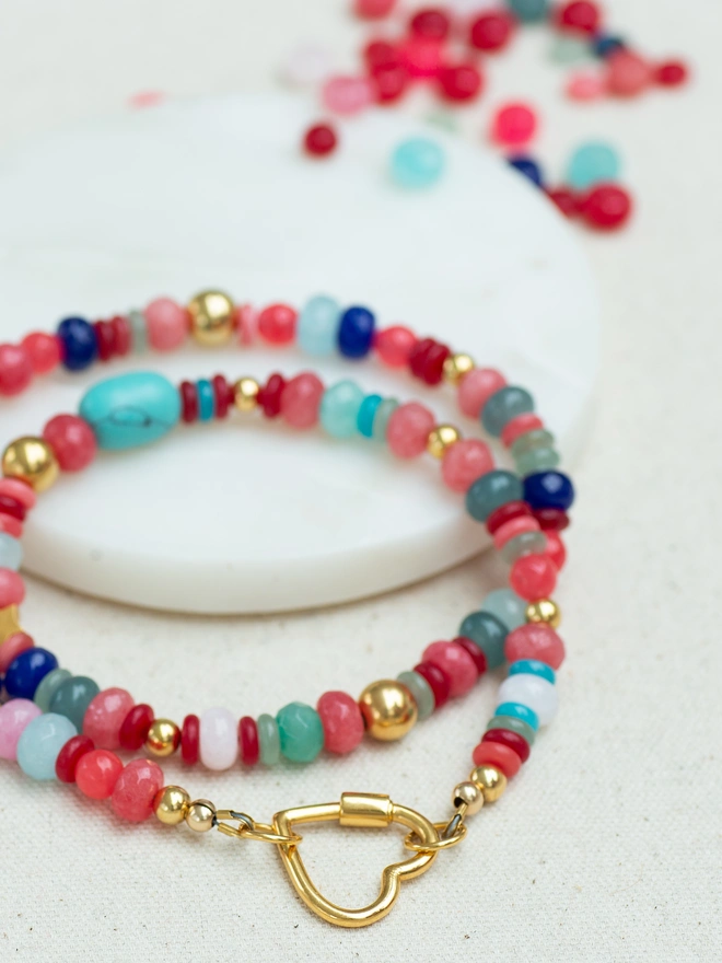 The Love Drunk Necklace is a vibrant jade and aqua agate bead necklace finished with warm gold plated accents and a statement heart-shaped carabiner. Bursting with colour and personality, this bold beaded necklace is designed to celebrate love, confidence and carefree summer energy — the perfect feel-good statement piece.