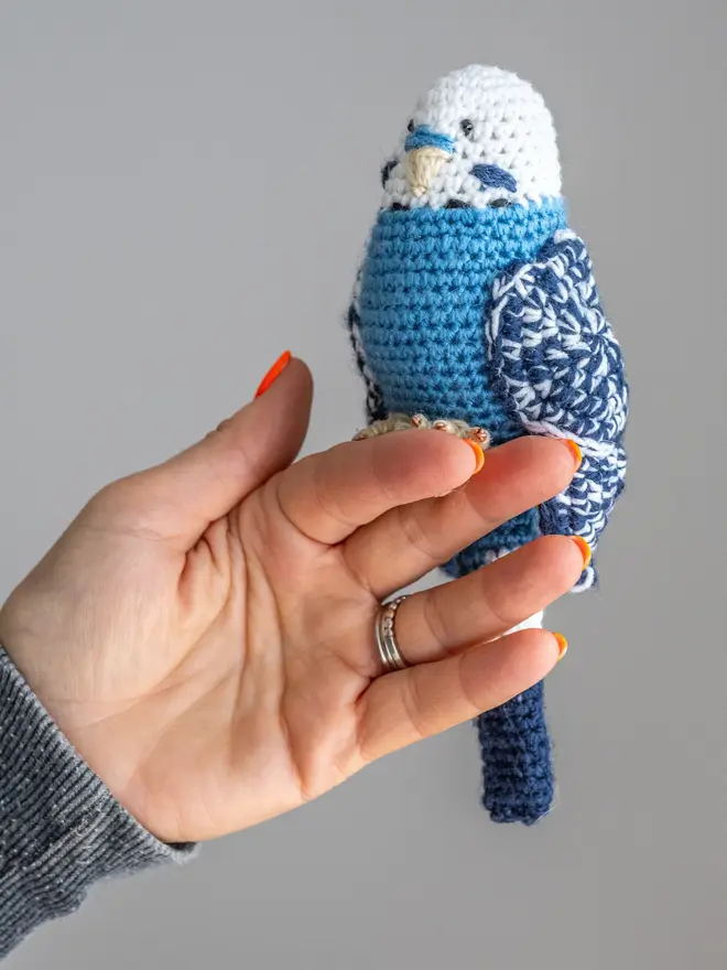 Budgerigar Hand Crocheted Figure, a blue  crocheted bird sitting on a wooden poll. 