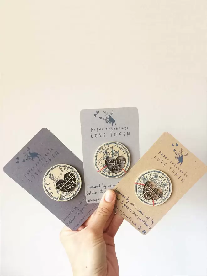 Fiona holds all three of the love token designs in the storm blue colour, on presentation cards