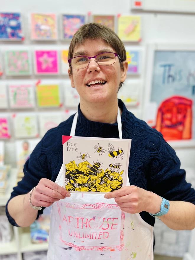 Artist holding riso printed charity card featuring a yellow & black Bee design & the words Bee Free