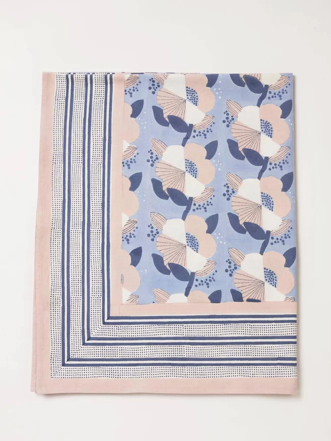 Blue tablecloth folded in hals and featuring a large scale block printed floral design in cream, navy and dusty pink colours