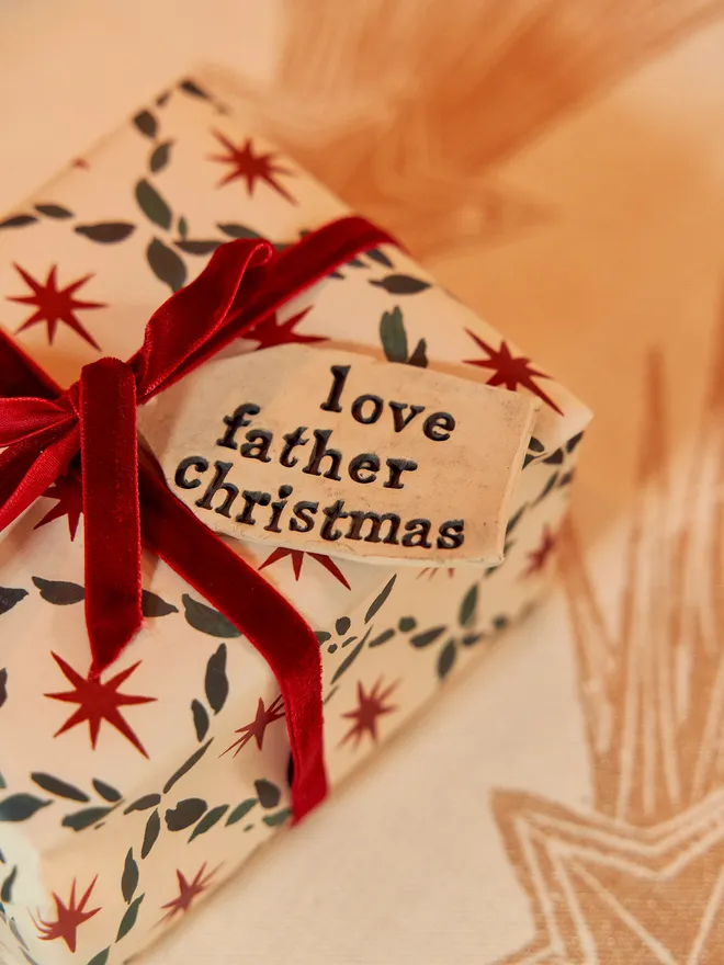 'Love Father Christmas' Handmade Ceramic Gift Tags, a ceramic gift tag attached to a gift