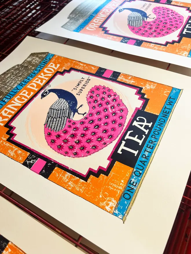 Orange Pekoe Peacock Tea Tin Screenprint Tip Top Tea, a colourful tea tin design on a white screenprint. It is placed on a studio rack. 