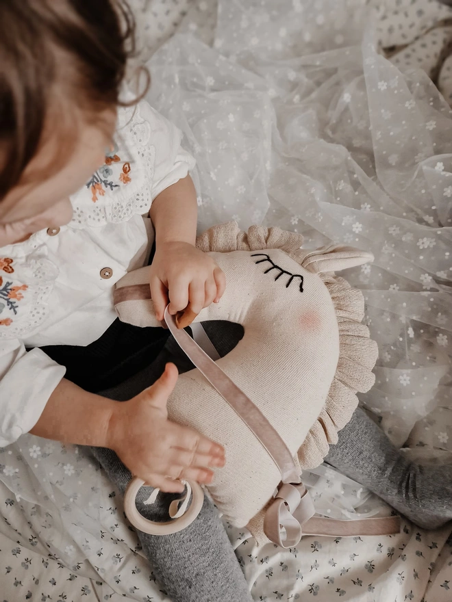 Horse Baby Rattle Toy, a child with a horse baby rattle toy in a bedroom surrounded by other bedroom accessories. 