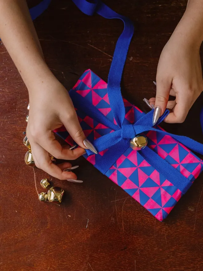 flouro pink and blue pattern tissue paper wrapped gift with blue ribbn and bells